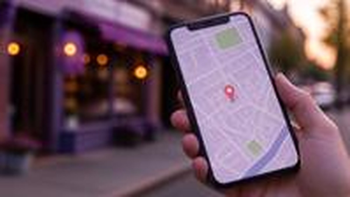 Mão segurando smartphone mostrando um mapa com pin de localização